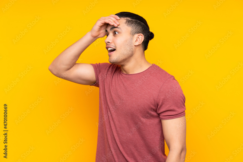 Asian handsome man isolated on yellow background surprised and sending a message Asian handsome man isolated on yellow background surprised and sending a message