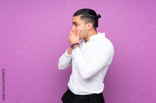 Asian handsome man isolated on blue background covering mouth and looking to the side photo