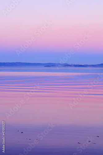 Colorful sunset sky with glowing pink clouds above the blue sea or ocean of fjord. Reflections on the water. Breathtaking scenery. Romantic landscape. Beauty in nature