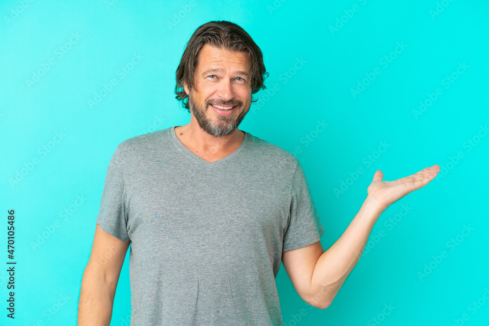 Senior dutch man isolated on blue background holding copyspace imaginary on the palm to insert an ad Senior dutch man isolated on blue background holding copyspace imaginary on the palm to insert an ad