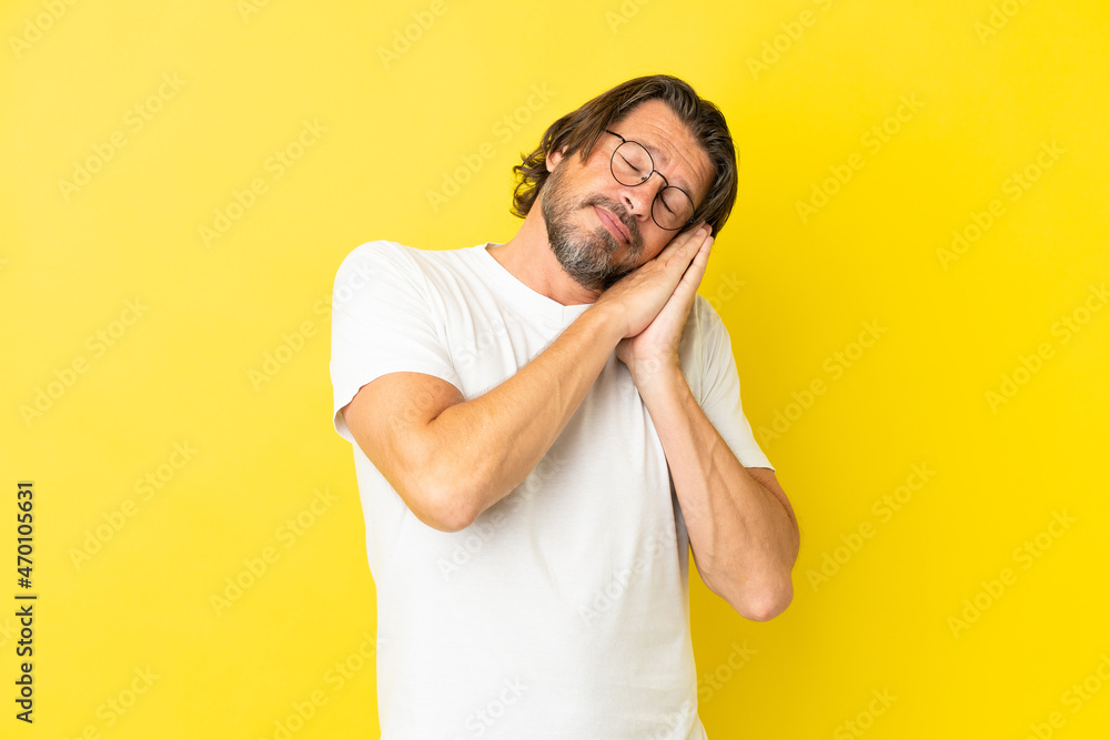 Senior dutch man isolated on yellow background making sleep gesture in dorable expression Senior dutch man isolated on yellow background making sleep gesture in dorable expression