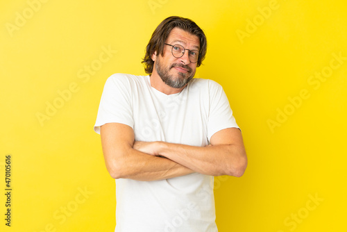 Senior dutch man isolated on yellow background making doubts gesture while lifting the shoulders