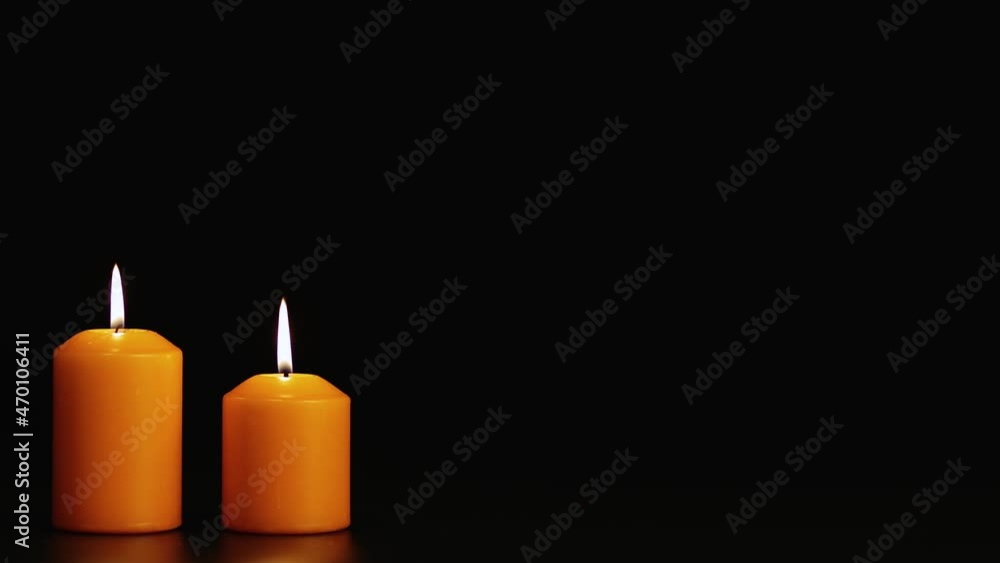 Two yellow mysterious burning candles on a black background. Copy space. Video screensaver