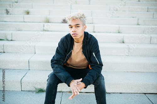 Foto Young latin american male sitting on stairs at the street