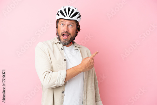 Senior dutch man with bike helmet isolated on pink background surprised and pointing side