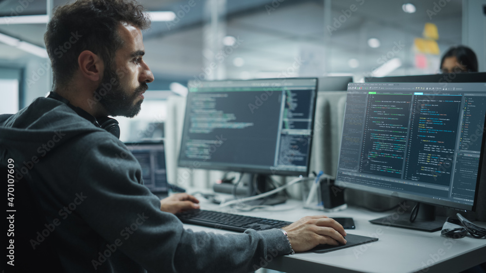 Diverse Office: IT Programmer Working on Desktop Computer. Male Specialist Creating Innovative Software Engineer Developing App, Program, Video Game. Terminal with Coding Language. Over Shoulder Diverse Office: IT Programmer Working on Desktop Computer. Male Specialist Creating Innovative Software Engineer Developing App, Program, Video Game. Terminal with Coding Language. Over Shoulder