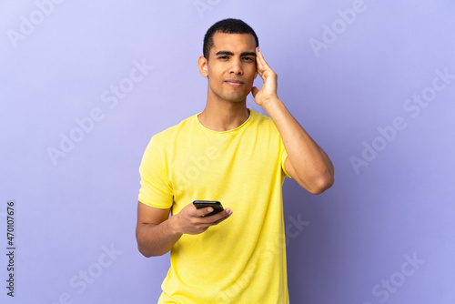 African American man over isolated purple background using mobile phone unhappy and frustrated with something. Negative facial expression