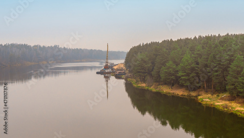 Floating crane on the river. Dredging crane working near shore. Conservation river flow. Nature, river, sky, clouds.
