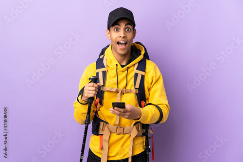 African American man with backpack and trekking poles over isolated background surprised and sending a message
