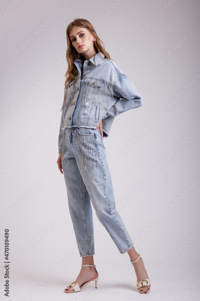 High fashion photo of a beautiful elegant young woman in a pretty denim jeans oversize jacket with rhinestones, pants posing over white, soft gray background. Slim figure. Studio Shot. High fashion photo of a beautiful elegant young woman in a pretty denim jeans oversize jacket with rhinestones, pants posing over white, soft gray background. Slim figure. Studio Shot.