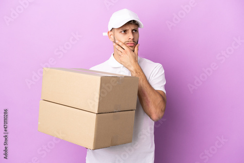 Delivery caucasian man isolated on purple background having doubts