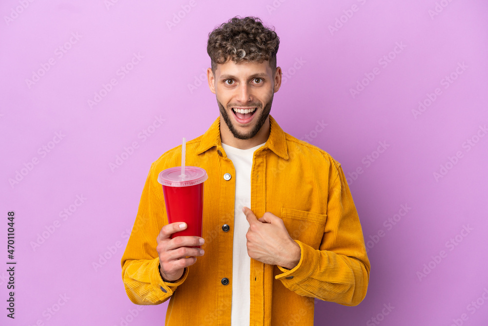Young blonde man holding soda isolated on purple background with surprise facial expression Young blonde man holding soda isolated on purple background with surprise facial expression