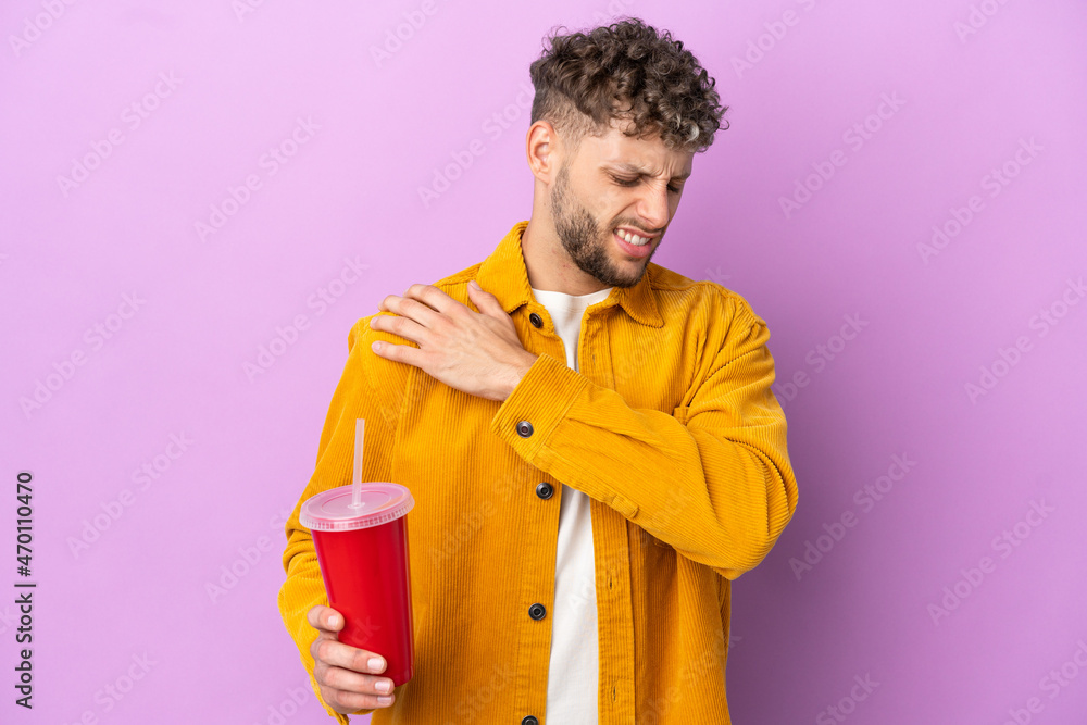 Young blonde man holding soda isolated on purple background suffering from pain in shoulder for having made an effort Young blonde man holding soda isolated on purple background suffering from pain in shoulder for having made an effort