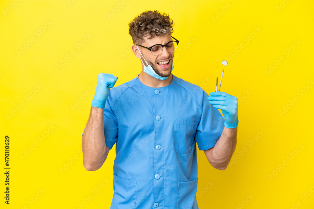 Dentist blonde man holding tools isolated on background celebrating a victory Dentist blonde man holding tools isolated on background celebrating a victory