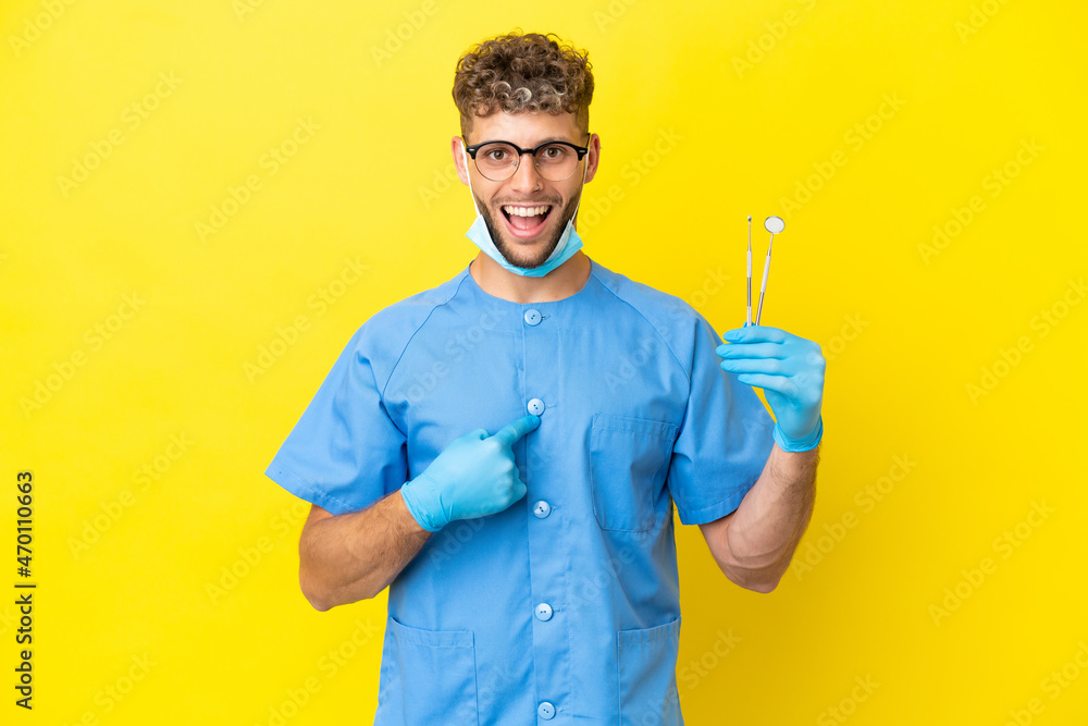 Dentist blonde man holding tools isolated on background with surprise facial expression Dentist blonde man holding tools isolated on background with surprise facial expression