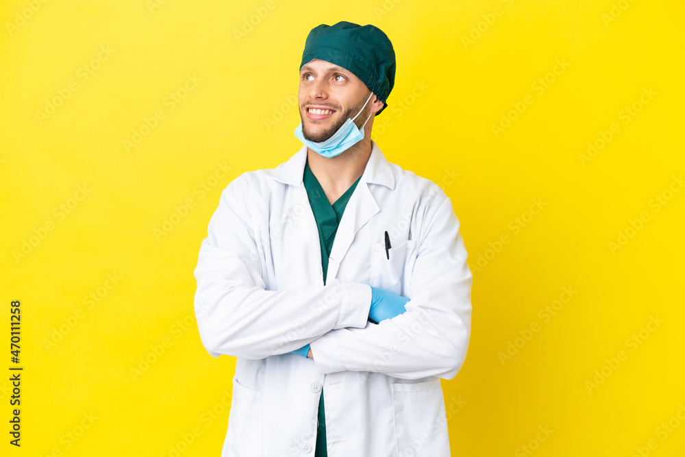 Surgeon blonde man in green uniform isolated on yellow background looking up while smiling Surgeon blonde man in green uniform isolated on yellow background looking up while smiling