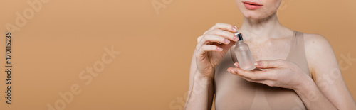 Cropped view of young woman holding bottle with cosmetic serum isolated on beige, banner