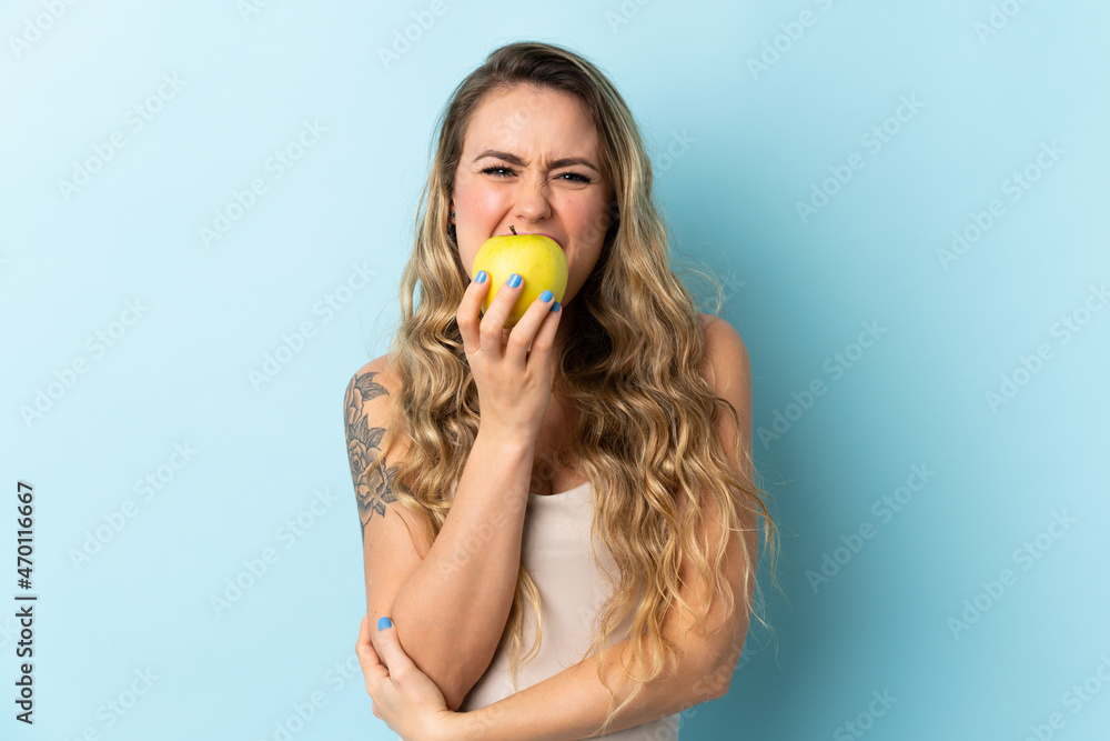 Young Brazilian woman isolated on blue background eating an apple Young Brazilian woman isolated on blue background eating an apple