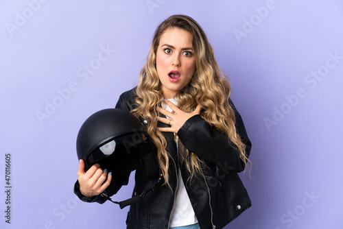 Young Brazilian woman holding a motorcycle helmet isolated on purple background surprised and shocked while looking right