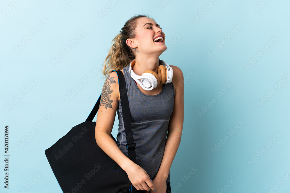 Young sport Brazilian woman with sport bag isolated on blue background laughing Young sport Brazilian woman with sport bag isolated on blue background laughing