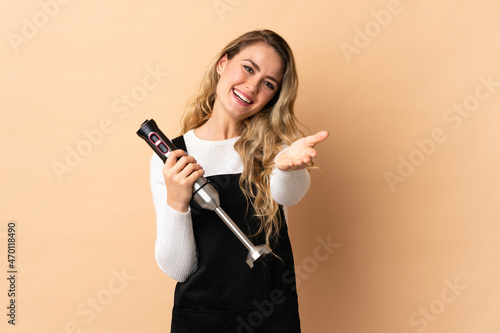 Young brazilian woman using hand blender isolated on beige background shaking hands for closing a good deal