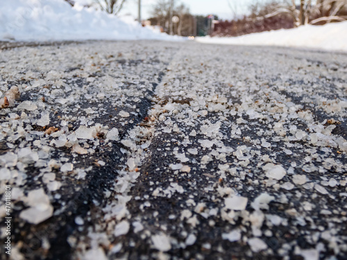 Salt grains on icy sidewalk surface in the winter. Applying salt to keep roads clear and people safe in winter weather from ice or snow