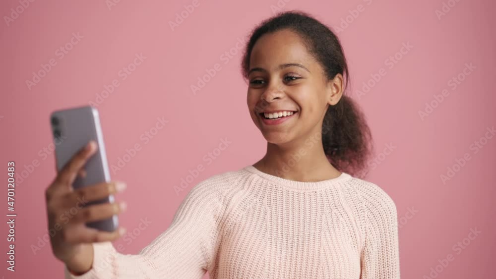 Positive African little girl talking by video call on the phone in the pink studio Positive African little girl talking by video call on the phone in the pink studio