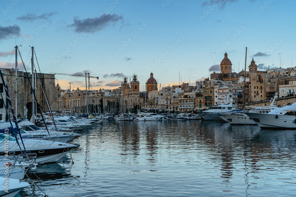 Luxury motor boats in Vittoriosa Yacht Marina at sunset.Holiday high class lifestyle travel concept.Boat trip in Mediterranean.View of expensive sailing yachts at pier,church old town in background.