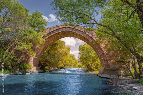 An ancient stone bridge over the blue river in the forest. Fairy tale background
