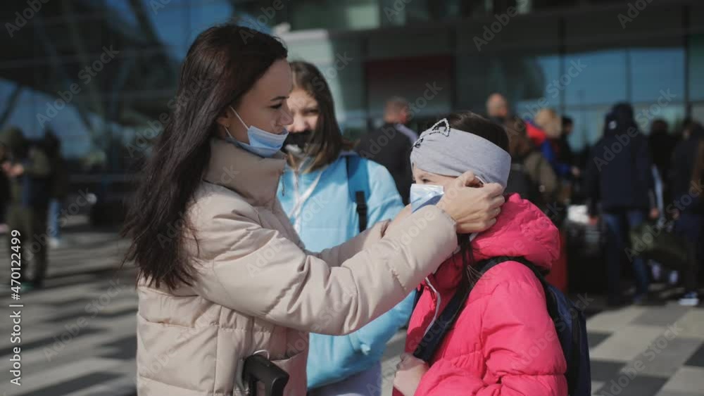 A woman puts a medical mask on her little daughter before entering the airport building. A woman puts a medical mask on her little daughter before entering the airport building.