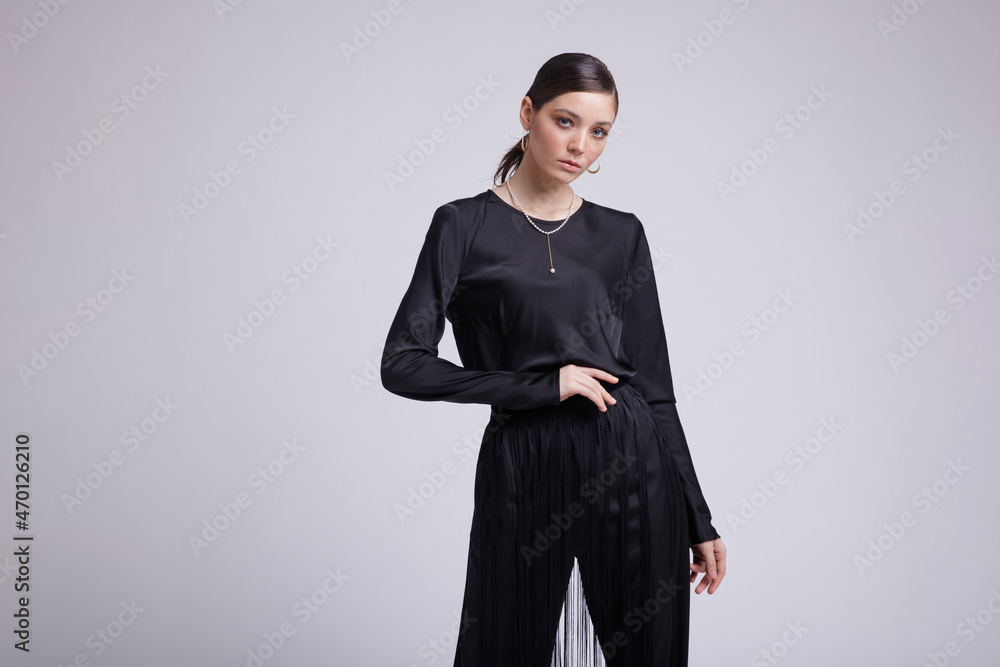 High fashion photo of a beautiful elegant young woman in a pretty black blouse, fringe trousers, accessories over white background. Studio Shot. Gathered dark hair. Slim figure High fashion photo of a beautiful elegant young woman in a pretty black blouse, fringe trousers, accessories over white background. Studio Shot. Gathered dark hair. Slim figure