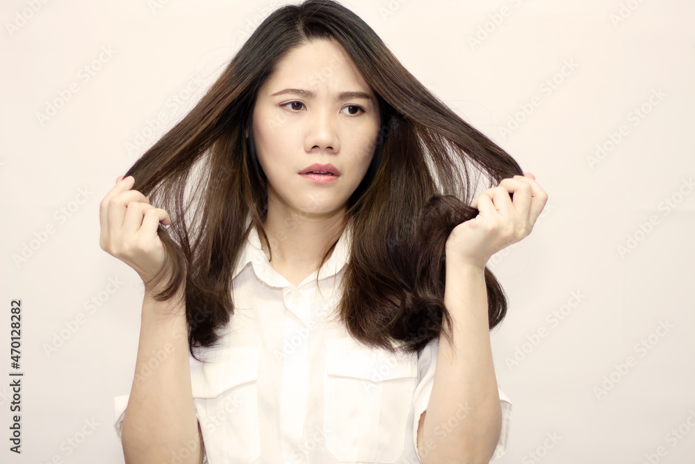 Asian beautiful women wear white t-shirt are holding and watching her hair with worry and unhappy cause by hair loss and dry or damage Asian beautiful women wear white t-shirt are holding and watching her hair with worry and unhappy cause by hair loss and dry or damage