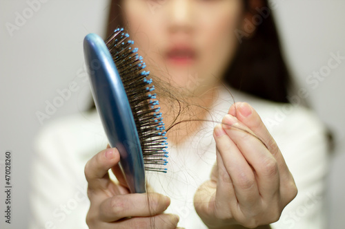 Asian woman look hair loss and taking hair from a blue comb