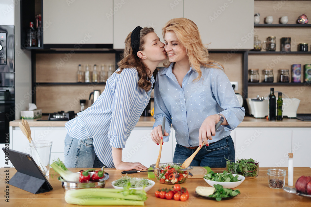 Mom and daughter cooking together in the kitchen. They use vegetables for cooking in a good mood, happy to be together