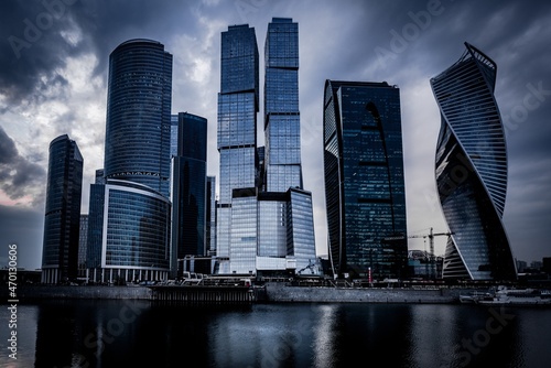 Low angle shot of grey skyscrapers in front of the river under the dark cloudy sky