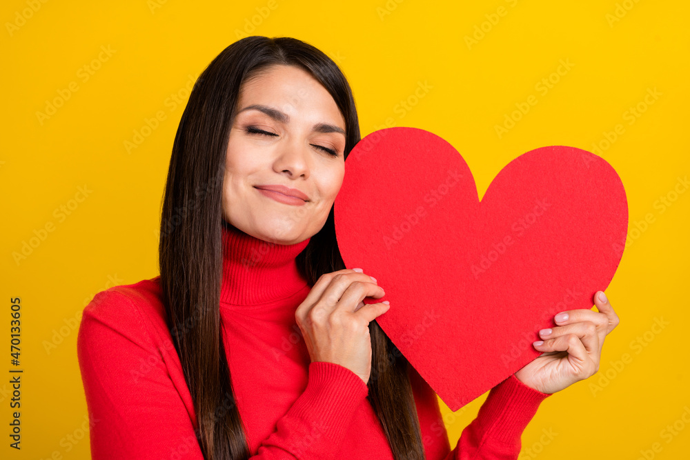 Portrait of adorable satisfied lady closed eyes hold hug heart postcard isolated on yellow color background Portrait of adorable satisfied lady closed eyes hold hug heart postcard isolated on yellow color background
