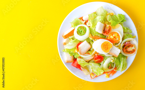 Delicious fresh vegetable salad on a white bowl on yellow background, top view.