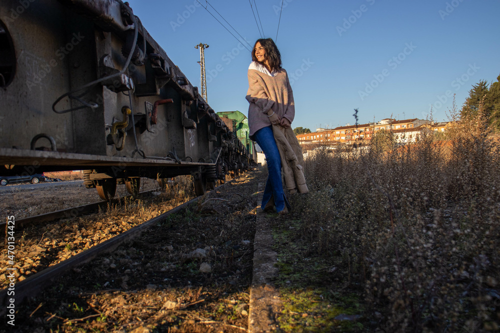 young brunette model on railroad tracks next to scrapped old freight train
