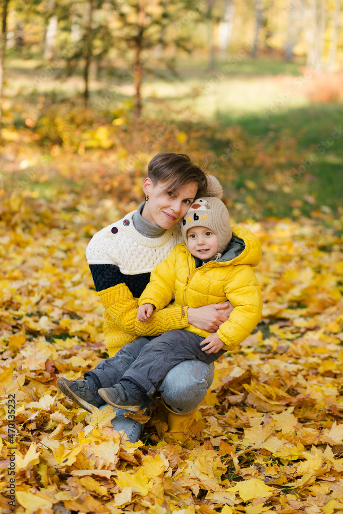 Mother and son looking at camera in autumn park among yellow leaves Mother and son looking at camera in autumn park among yellow leaves