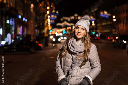 portrait of a beautiful young woman walking in the winter along the evening street in the lights. near the lights from the cars