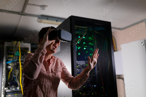 Caucasian woman smiling while wearing vr headset touching an invisible screen in server room photo