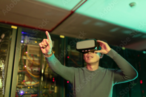 Asian man wearing vr headset touching an invisible screen in computer server room