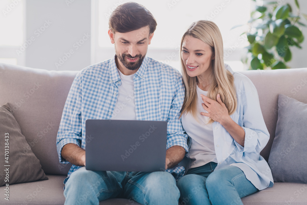 Photo of positive lover couple two people sit divan read email netbook wear casual outfit in comfortable home indoors Photo of positive lover couple two people sit divan read email netbook wear casual outfit in comfortable home indoors