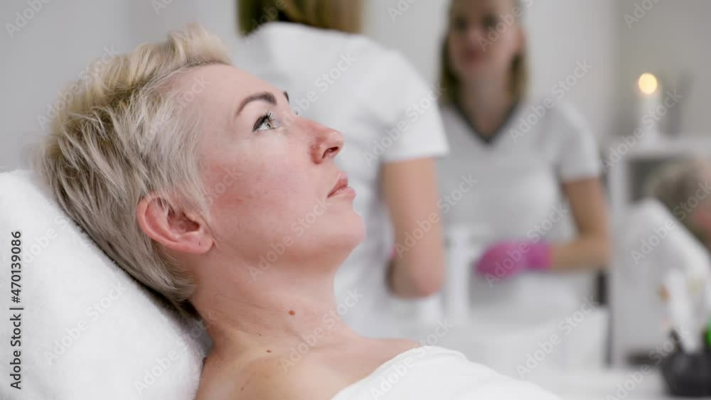 Professional cosmetology. A client lying on a coach at beauty salon. A woman's face in close-up. In the background, the cosmetologist is preparing for the procedure. Slow motion. Professional cosmetology. A client lying on a coach at beauty salon. A woman's face in close-up. In the background, the cosmetologist is preparing for the procedure. Slow motion.