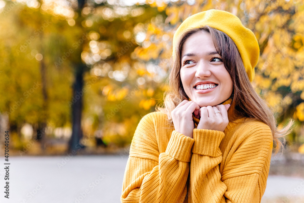 Portrait of a young beautiful woman in a yellow sweater smiling and looking away. Nice sunny autumn weather. A girl walks alone in the park. Discounts and sale Portrait of a young beautiful woman in a yellow sweater smiling and looking away. Nice sunny autumn weather. A girl walks alone in the park. Discounts and sale