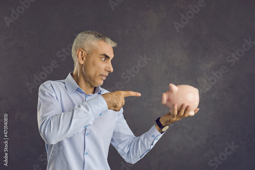 Middle-aged man isolated on black studio background hold piggybank think of financial investments. Pensive male consider manage budget or plan expenses expenditures. Finance, economy, savings concept. photo