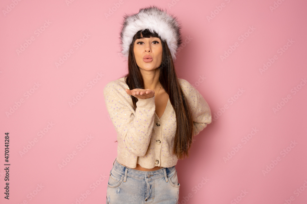 Beautiful young woman with long hair in winter clothing sending air kiss isolated over pink background. Beautiful young woman with long hair in winter clothing sending air kiss isolated over pink background.