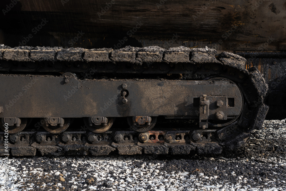 A fragment of a tracked bulldozer for laying asphalt. Tracks stained with asphalt and bitumen
