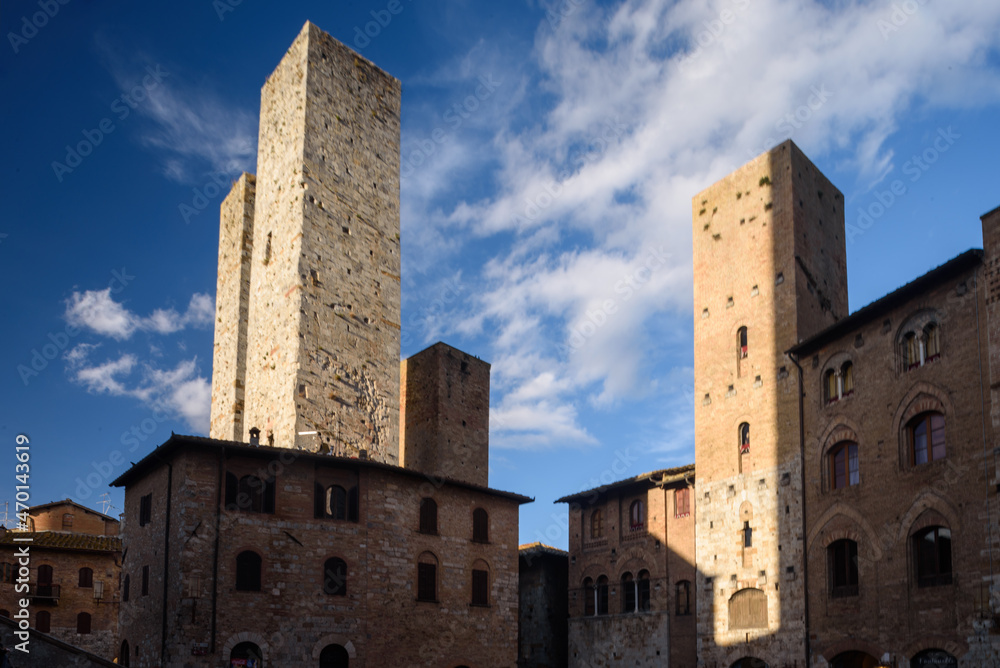 Geschlechtertürme, San Gimignano, Toskana, Italien bei Himmel mit Wolken und Sonne und Schatten.