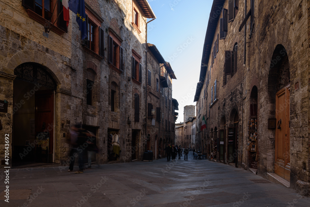 Gasse in San Gimignano i schatten mit Fassaden und Personen bei blauem Himmel